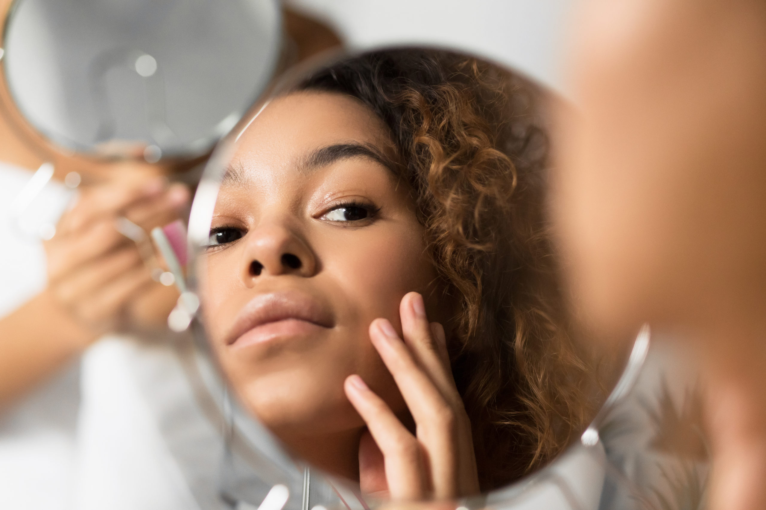 a woman examines her face in a mirror after receiving an eye bag treatment