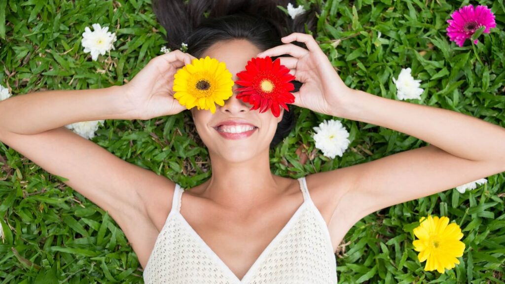 Girl in the grass covering her eyes with flowers