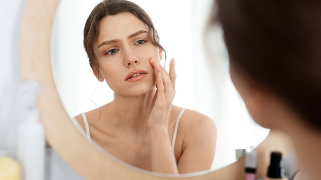 woman looking at skin in mirror